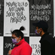 People wearing facemasks walk past posters created by thelockerroomnyc in New York City on February 5, 2021
